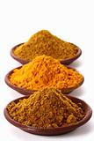 piles of bright Curry Powder and tumeric in teracotta dish on wh