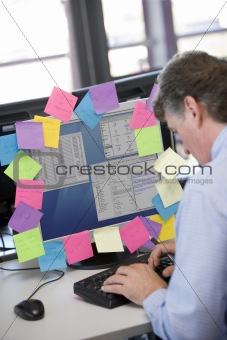 Businessman working at computer covered in reminder notes