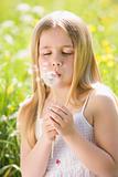 Young girl in field blowing dandelion