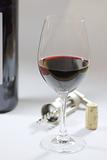 a glas of red wine and a wine bottle, the cork and the corkscrew