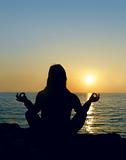 Woman silhouette making yoga over sunset sea background
