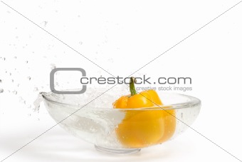 Yellow paprika falling into glass vase with water