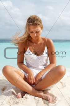 Woman in meditation on white sand beach.