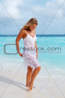 Woman in wet gauzy dress on white sand beach.