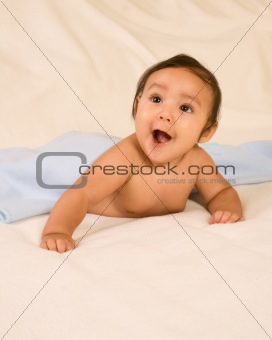 Excited ethnic baby boy lying down on blanket