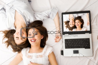 Two Young girls relax with laptop lying on the floor