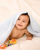 ethnic baby boy with toy lying under blanket
