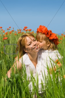 Little girl kissing her mother on the poppy field