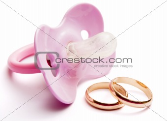 Baby pacifier and wedding rings, conceptual