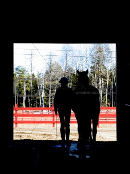 horse and rider exiting the barn in silhouette