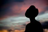 Woman in a cowboy hat silhouetted against a sunset sky.