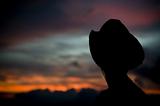 Woman in a cowboy hat silhouetted against a sunset sky.