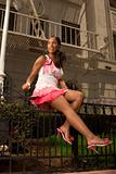 Black woman in pink skirt sitting on forged fence