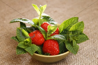 strawberry and mint leaves in bowl on burlap canvas background